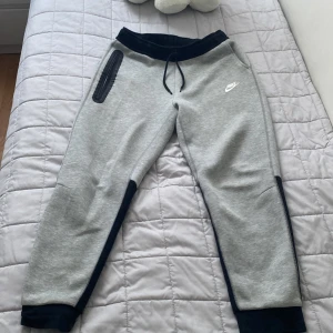 Nike grå mjukisbyxor XL - Snygga grå mjukisbyxor från Nike i storlek XL, med svarta detaljer vid midja och benslut. Byxorna har snörning i midjan, sidofickor och en vit Nike-logga på låret. Perfekta för chill eller träning, tillverkade i mjukt bomullsmaterial.