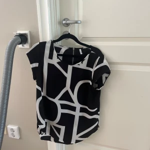 Svartvit blus från ONLY med grafiskt mönster - Säljer en svartvit blus från ONLY i storlek 36. Blusen har ett coolt grafiskt mönster i vitt på svart botten, rund halsringning och korta ärmar. Dragkedja bak för en snygg detalj. Perfekt för dig som gillar statement-plagg!