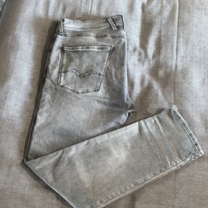 Replay Anbass  - Säljer ett par Replay Anbass jeans i snyggt grått tvättat denim. Klassisk femficksmodell med raka ben och diskreta detaljer på bakfickorna. Jeansen har normal passform och är tillverkade i mjukt bomullsmaterial med lite stretch för extra komfort. Jeansen är använda ett par gånger men är i toppskick förutom en liten skada som är på patchen men det går att fixa, köpta i butik det är bara att skriva vid frågor osv 😁