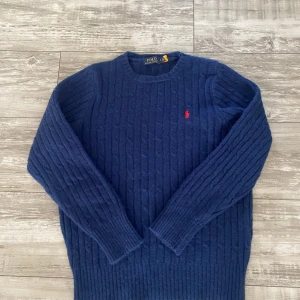 Marinblå stickad tröja Polo Ralph Lauren - Snygg marinblå stickad tröja från Polo Ralph Lauren i storlek S. Tröjan har ett klassiskt kabelstickat mönster och en röd broderad logga på bröstet. Rund hals och långa ärmar, perfekt för att hålla värmen under kyliga dagar. Använd typ 2 gånger. Passar folk som är 13-14år.
