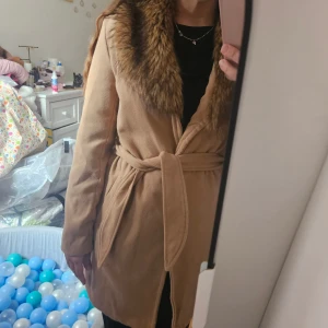 Beige kappa med fuskpäls från YOINS - Säljer en snygg beige kappa från YOINS med bred krage i fuskpäls och knytskärp i midjan. Knappt använd så väldigt fint skick. Storlek M, men något liten i storlek så därför har jag satt S som storlek 