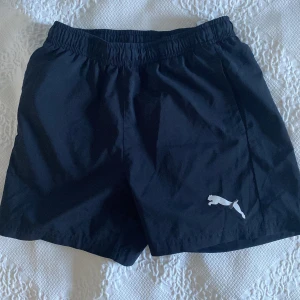 Svarta träningsshorts från Puma - Svarta shorts från Puma med elastisk midja och klassisk vit Puma-logga på benet. Perfekta för sport eller chill. Snygg enkel design som funkar till allt.