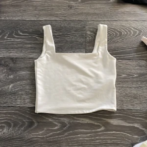 Vit linnetopp från Amisu XS - Säljer en stilren vit linnetopp från Amisu i storlek XS. Toppen har breda axelband och en rak, croppad passform som ger en clean look. Materialet är mjukt och har en lätt glansig finish, perfekt för att matcha med jeans eller kjol.