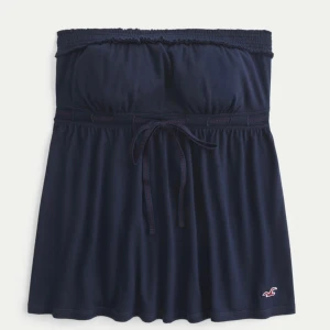 Mörkblå babydoll top från Hollister S - Supersöt mörkblå babydoll top från Hollister, limited edition. Toppen har resår i midjan, knytband och en liten broderad logga nertill. Tillverkad i mjuk bomull, perfekt för sommarens alla äventyr. Enkel och stilren design som är lätt att matcha. Det finns avtagbara axelband om man inte vill bära toppen axelbandslös.