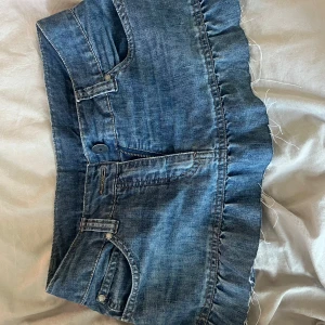 Blå jeanskjol med volangkant - Snygg blå miniskirt i jeans med volangkant nertill. Kjolen har klassiska fickor fram och bak, samt coola broderade detaljer på bakfickorna. Den är i storlek 38 men passar även dig som har storlek 36! Pris kan diskuteras