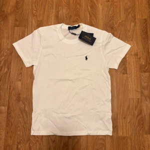 Vit t-shirt från Polo Ralph Lauren - Helt ny! - Vit t-shirt från Polo Ralph Lauren med den klassiska loggan broderat i svart. | Skick: 10 / 10 - helt ny! | Storlek: S | Nypris: ~ 1000 | Vårt pris: 599 | Tveka inte att höra av er med funderingar eller fler bilder! Priset kan absolut förhandlas!