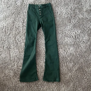 Gröna bootcut byxor från Zara - Snygga gröna bootcut byxor från Zara med hög midja och fyra silvriga knappar framtill. Byxorna har stora fickor fram och klassiska bakfickor. 