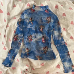 Blå mesh polotröja med änglar - En blå polotröja från SHEIN i mesh med moln och änglar. Tröjan är långärmad och har en tight passform med hög krage. Strl XS!💞                    OBS: see-through