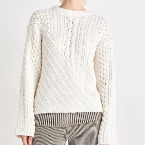 Vit stickad tröja med kabelmönster - Säljer en vit stickad tröja med snyggt kabelmönster och rund hals. Tröjan har långärmade ärmar och en cool mix av diagonala och vertikala stickningar som ger en unik look. Perfekt för dig som gillar klassisk stil med en twist. Använd 1 gång!