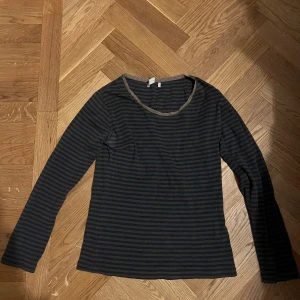 brun och svart randig långärmad tröja - Säljer en långärmad tröja från H&M i mörkblått och svart med smala ränder. Tröjan har en rund halsringning med en liten spetskant som detalj. Perfekt för dig som gillar enkel och stilren design med en twist. Passar dig som vill ha en skön och snygg vardagströja.