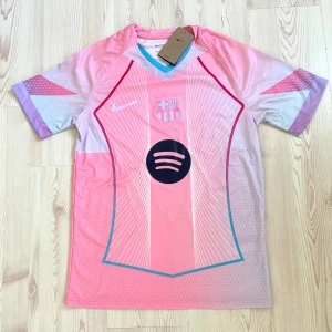 Special  Barcelona Nike fotbollströja - Snygg Barcelona fotbollströja från Nike i rosa med ljusblå och lila detaljer. Tröjan har vita tunna ränder, klubbmärke och Nike-logga i holografisk stil samt Spotify-logga på bröstet. Tillverkad i lätt och ventilerande polyester, perfekt för match eller träning.