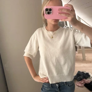 Vit stickad tröja med kort ärm - Snygg vit stickad tröja med korta ärmar och rund hals. Tröjan har ribbade muddar vid ärmslut och nederkant, vilket ger en clean och enkel look. Perfekt att matcha med jeans eller kjol för en chill stil.