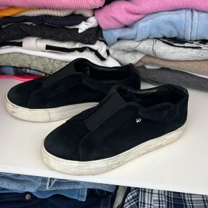 Svarta mocka sneakers med platt sula - Svarta sneakers i mocka med bred resår över foten för enkel påtagning. Snygg minimalistisk design och vit platt sula som ger en clean look. Perfekta för dig som gillar stilrena och bekväma skor till vardags. Passar till jeans, kjol eller shorts.