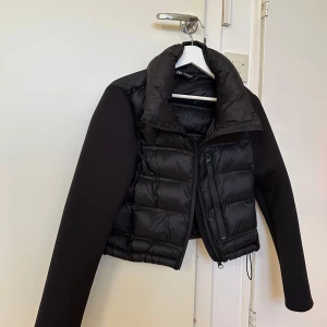 Svart dunjacka från Zara  - Säljer en svart dunjacka från Zara med hög krage och dragkedja framtill. Jackan har annat material i ärmarna och är croppad i modellen. Perfekt att slänga över en hoodie eller långärmad tröja för en cool layering-effekt. Passa på då det är frifrakt idag!