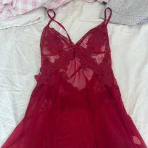 Röd spetsklänning, lingerie med tunna axelband - Säljer en kort röd / vinröd klänning, nattlinne, lingerie med tunna axelband och transparent mesh. Klänningen har vackra spetsdetaljer med blommönster och en liten rosett framtill. Perfekt för dig som gillar romantisk och feminin stil. Helt ny, aldrig använd! KÖPT FÖR 400KR