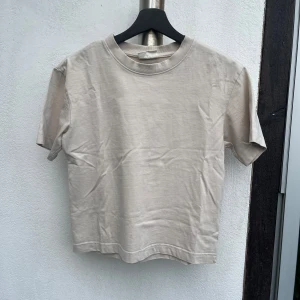 Beige Gina t-shirt - En vanlig basic beige t-shirt från Gina Tricot. Modellen är rak och har korta ärmar samt rund hals med ribbad kant. Materialet är mjuk bomull. Använd en del men fortfarande i fint skick. Storlek XS. (nypris 169kr)