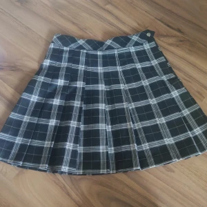 Svartvit rutig kjol från H&M Divided - Supersnygg svartvit rutig kjol från H&M Divided i kort modell. Kjolen är plisserad och har en knappdetalj i midjan. Perfekt för dig som gillar en klassisk men edgy stil. Materialet känns mjukt och följsamt.