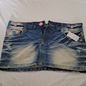 Blå och ljusblå jeans miniskirt - Söt miniskirt med olika nyanser av blå. Rosa detaljer såsom knappar och text. Köpt från en marknad i Thailand.