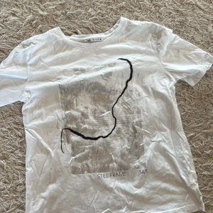 Vit t-shirt med print från Zara - Vit t-shirt från Zara med coolt abstrakt print i silver och svart på framsidan. Rund hals och korta ärmar, tillverkad i mjuk bomull. Texten 'STILL FRAME 34/1' syns nedtill på trycket. Slutsåld.