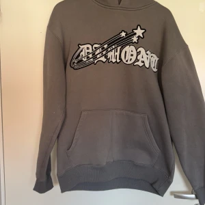 Grå hoodie från Belmont med tryck /de ser ut som den är röd på bilden men den är inte de i värkligheten!! - Säljer en grå hoodie från Belmont med stort vitt och svart tryck på bröstet och coola stjärndetaljer. Tröjan har huva, magficka och långa ärmar med ribbade muddar. Perfekt för chill dagar och streetwear-stil.