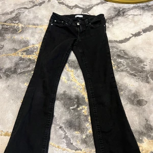 Svarta bootcut jeans från Gina tricot - Svarta jeans från Gina tricot i bootcut-modell med snyggt utsvängda ben. Klassisk femficksdesign med två bakfickor som har lock och silverfärgade knappar. Jeansen har normal passform och är tillverkade i mjukt denimtyg som sitter skönt hela dagen.