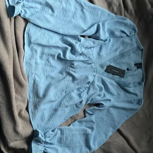 Ljusblå blus från Vero Moda - Supersöt ljusblå blus från Vero Moda med v-ringad hals och spetsdetaljer. Blusen har långärmade puffärmar med resår vid ärmslut. Pris går självklart alltid att diskutera💕
