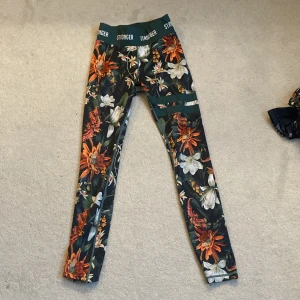 Blommiga leggings från Stronger  - Snygga leggings från Stronger i storlek XS med blommigt mönster i orange, vitt och grönt.