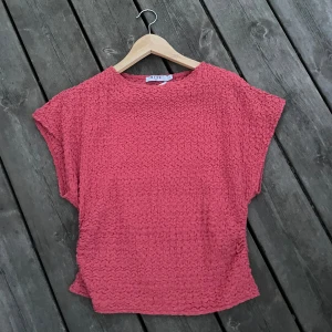 Rosa strukturerad topp från NA-KD - Säljer en rosa topp från NA-KD i storlek 38. Toppen har en cool, strukturerad yta och är kortärmad med loose passform. Perfekt för dig som gillar att sticka ut med färg och textur. Enkel rund halsringning och mjukt material.