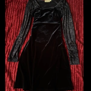 Svart sammetsklänning Hennes Collection - Supersnygg svart sammetsklänning från Hennes Collection i storlek 38. Klänningen har långärmade, lätt glansiga ärmar och en mjuk, figurnära passform med något utsvängd kjol. Perfekt för dig som gillar en elegant och lite mystisk vibe. Har sytt in vid bröstet, går att lösa upp. 💖💖💖 Klänninger skimmrar i mörknblått. 