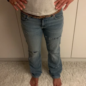 Ljusblå slitna jeans med låg midja - Säljer ett par ljusblå jeans med låg midja och rak passform. Jeansen har slitna detaljer och fransiga hål på låren, samt rå kant upptill. Klassisk femficksmodell med dragkedja i gylfen. Perfekta för en chill och avslappnad stil. Midjemått: 40cm . Jag klippte knappen av på jensen  