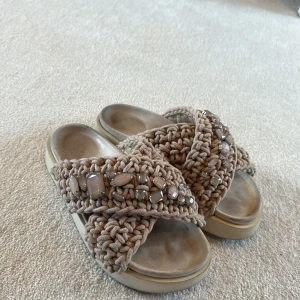 Inuikii Beige sandaler med pärlor och plattsula - Säljer ett par chunky sandaler i beige med breda, grovstickade band dekorerade med pärlor och stenar. Sandalerna har en platt sula och öppen tå, perfekt för dig som gillar boho-vibe och vill sticka ut med coola detaljer. 