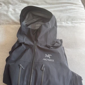 Svart vindjacka  Arc'teryx alpha sv M - Arc'teryx Jacka - Storlek Medium - Nästan Oanvänd  Säljer min Arc'teryx jacka i storlek Medium. Jag är 183 cm lång och har använt den mycket sparsamt – mest när det regnat eller vid slalomåkning. Jackan är i mycket bra skick och ser nästan ny ut, då den bara använts vid specifika tillfällen.   Jag säljer den eftersom jag inte har behov av den längre. Tyvärr har jag inte kvar kvittot pga köpt den online, men jag har kvar taggen från jackan.  Pris: 2500  Hör av dig om du är intresserad 