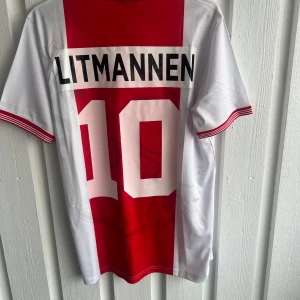 Ajax Litmanen 10 fotbollströja Umbro M - Ajax fotbollströja med Litmanen 10 på ryggen, tillverkad av Umbro. Klassisk design med bred röd mittpanel och vita sidor, samt vita tryck och klubbmärke. Krage med röda och vita ränder, samt röda detaljer på ärmslut. Materialet är lätt och andas, perfekt för match eller träning.