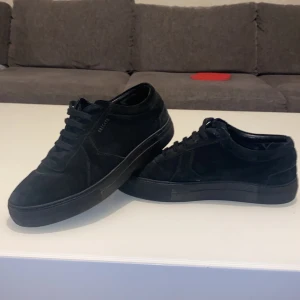Svarta mocka sneakers från arigato  - Snygga svarta sneakers från arigato i mjuk mocka med platt sula och rund tå. Skorna har klassisk snörning och en stilren, minimalistisk look som passar till jeans eller chinos. Perfekta för dig som gillar enkel och clean stil.