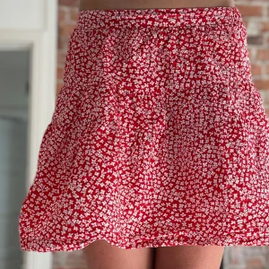 Röd blommig kortkjol från Zara - Superfin röd kortkjol från Zara med vitt blommigt mönster. Kjolen har en luftig och lätt form med resår i midjan för skön passform. Perfekt för dig som gillar färg och mönster! Materialet känns mjukt och svalt mot huden.