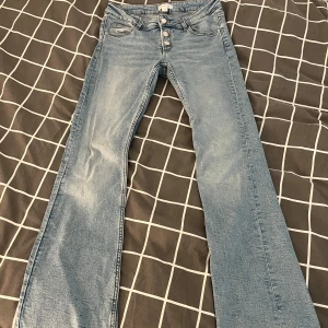 Bootcut jeans från Gina Young ljusblå - Snygga ljusblå bootcut jeans från Gina Young i storlek 158. Jeansen har hög midja, klassisk femficksdesign och knäppning med tre silverfärgade knappar. Materialet är mjukt denim och insidan har justerbar midja med knapp. Innerbenslängd 75