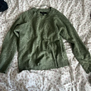 Grön stickad tröja  - Mysig grön stickad tröja med rund hals och långa ärmar. Tröjan har ribbade muddar vid ärmslut och nederkant, perfekt för att hålla värmen under kyliga dagar. Enkel och stilren design som passar till jeans eller kjol.
