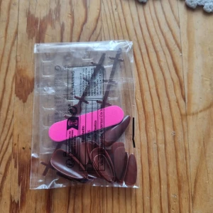 Bruna lösnaglar med rosa fil - Säljer ett set med bruna lösnaglar i oval form, perfekt för att fixa snygga naglar hemma. Medföljer en liten rosa nagelfil för att forma naglarna precis som du vill. Naglarna är gjorda av plast och kommer i en genomskinlig förpackning.