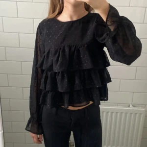 Glittrig volangblus - Jätte gullig svart blus med flera volanger & små glitterprickar. Endast använd 2-3 gånger 💗 (storlek 158/164 men sitter som XS) Perfekt till till exempel nyår