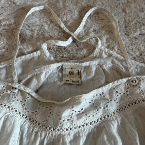 Spets linnetopp Xoye - Supersöt vit linnetopp från Xoye med tunna axelband som korsas i ryggen. Aldrig använd men köpt second hand! Inga defekter!