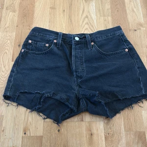 Svarta Levi's 501 jeansshorts W27 - Svarta jeansshorts från Levi's modell 501 med hög midja och råa, fransiga kanter. Klassisk femficksdesign, silverfärgad knapp och nitar, samt Levi's patch bak. Använda ca 3 gånger . Köpa i usa 