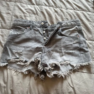Grå jeansshorts med fransad kant/slitningar - Säljer gråa jeansshorts midrise från zara. De är aldrig använda men köpta med slitningar/ fransar. Storlek 38 