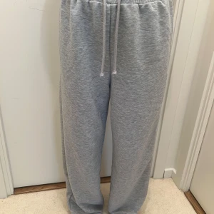 Grå mjukisbyxor med snörning - Säljer ett par grå mjukisbyxor med bred passform och snörning i midjan. Byxorna är tillverkade i mjukt bomullsmaterial och har en loose fit som ger en chill och avslappnad vibe. Perfekta för att hänga hemma eller dra till gymmet.