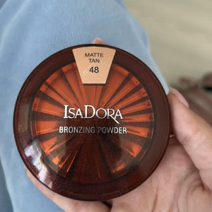 IsaDora Bronzing Powder Matte Tan 48 - IsaDora Bronzing Powder i nyansen Matte Tan 48. Kompakt bronzer med matt finish, perfekt för att ge ansiktet en solkysst look. Rund dosa i brunt plastmaterial med spegel i locket. Färgen är varm och naturligt tan, passar för contouring eller all-over glow.
