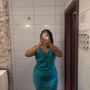 Turkos långklänning med v-ringning - Säljer en turkos långklänning med smala axelband och snygg v-ringning framtill. Klänningen är figurnära med slät yta. Använd endast en gång 