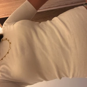 Vit topp med guldknappar - Supersnygg vit stickad topp med korta ärmar och rund hals. Baksidan har tre blanka guldknappar som ger en lyxig touch. Mjuk och skön kvalitet, perfekt till jeans eller kjol. Ribbad kant vid ärmslut och nederkant för extra stilpoäng.