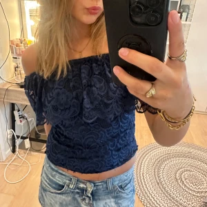 Mörkblå offshoulder spetsblus - Säljer en mörkblå offshoulder blus med snygg spets och blommigt mönster. Toppen är croppad och har korta ärmar som sitter snyggt över axlarna. Perfekt för dig som vill ha en romantisk och trendig look med lite extra detaljer.