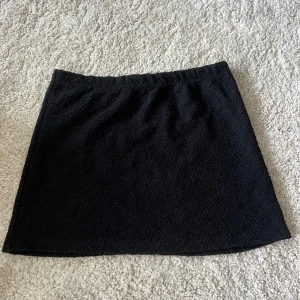 Svart kortkjol  - Svart kortkjol från Primark i storlek XS. Kjolen har ett diskret strukturerat mönster i tyget som ger en snygg touch. Enkel och stilren modell med rak passform, perfekt att matcha med en cool topp eller oversized hoodie.