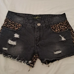 Leopard low waist jeansshorts  - As coola svarta jeansshorts med leopard mönster detaljer och slitna detaljer. Storleken är lite oklar men skulle säga 34/36. Köpt från en marknad i Thailand.
