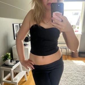 Tubtopp - Snygg svart croppad tubtopp med hjärtformad urringning. Toppen är axelbandslös och sitter tight mot kroppen, perfekt för att skapa en clean och stilren look. Materialet känns mjukt och stretchigt, vilket gör den bekväm att bära hela dagen. Hör av dig vid frågor.🤩